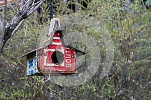 Birdhouse made with various old license plates hanging from a tree