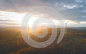 Birds eye view of wind turbines in the mountains under the cloudy sky at sunset