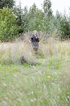 Birds watcher hidden in dry grass, mature woman with binoculars in hand, natural scientist