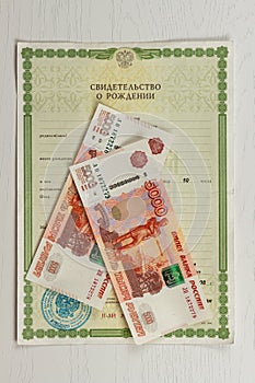 Birth certificate and paper money lie on a white wooden table