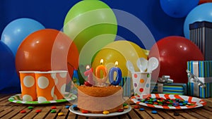 Birthday 100 cake on rustic wooden table with background of colorful balloons, gifts, plastic cups, plastic plate
