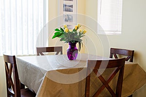 Birthday bunch of yellow roses in a purple vase on a dining room table