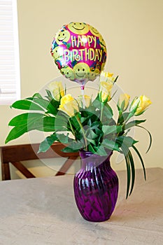 Birthday bunch of yellow roses in a purple vase in front of window