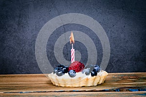 Birthday cake with berries and one burning candle