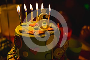 Birthday cake with burning candles and age 6 candle in the dark background with candies in decor