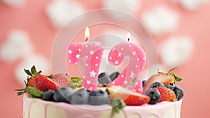 Birthday cake candle number 72. Candle and cake on pink background and fire by lighter. Close-up and slow motion