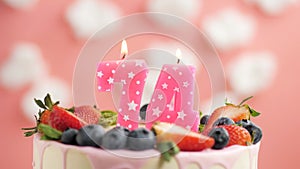 Birthday cake candle number 74. Candle and cake on pink background and fire by lighter. Close-up and slow motion