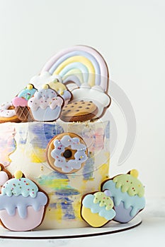 Birthday cake with colorful cream cheese frosting decorated with cookies. Gingerbread cookies in the shape of rainbow, cupcakes,