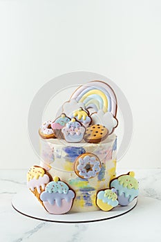 Birthday cake with colorful cream cheese frosting decorated with cookies. Gingerbread cookies in the shape of rainbow, cupcakes,