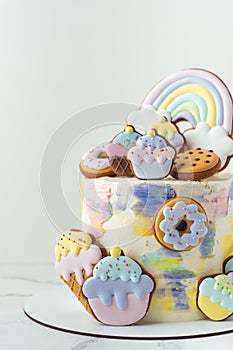 Birthday cake with colorful cream cheese frosting decorated with cookies. Gingerbread cookies in the shape of rainbow, cupcakes,