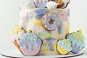 Birthday cake with colorful cream cheese frosting decorated with cookies. Gingerbread cookies in the shape of rainbow, cupcakes,