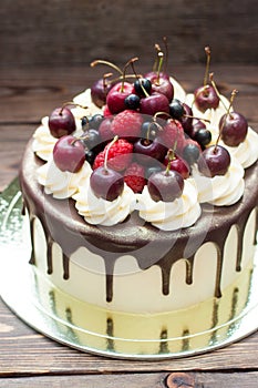 Birthday cake decorated with melted chocolate, whipped cream and fresh cherries. Rustic wooden background.