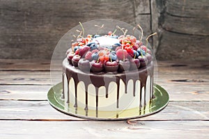 Birthday cake with melted chocolate, fresh cherry, raspberry, strawberry, red currant, blueberry on wooden background