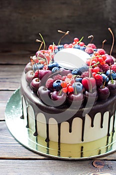 Birthday cake with melted chocolate, fresh cherry, raspberry, strawberry, red currant, blueberry on wooden background