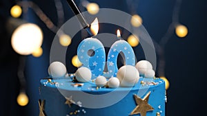 Birthday cake number 90 stars sky and moon concept, blue candle is fire by lighter. Copy space on right side of screen. Close-up