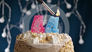 Birthday cake with 44 number pink candle on blue backgraund. Candles are set on fire