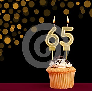 Birthday candle with cupcake - Number 65 on black background with out of focus lights