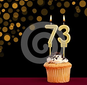 Birthday candle with cupcake - Number 73 on black background with out of focus lights