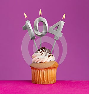 Birthday candle number 104 with cupcake on violet background