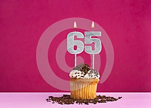 Birthday celebration with candle number 65 - Chocolate cupcake on pink background