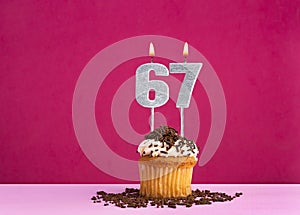 Birthday celebration with candle number 67 - Chocolate cupcake on pink background