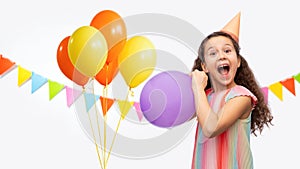 funny girl in birthday party hat blowing balloon