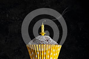 Birthday cupcak in paper cup with extinguished candles on a dark background