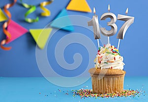 Birthday cupcake with candle number 137 - Blue background