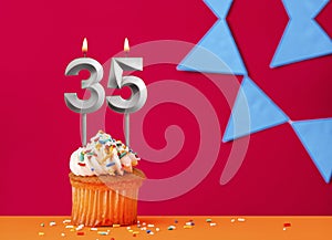 Birthday cupcake with candle number 35 on a red background with blue pennants