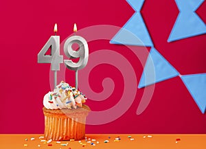 Birthday cupcake with candle number 49 on a red background with blue pennants
