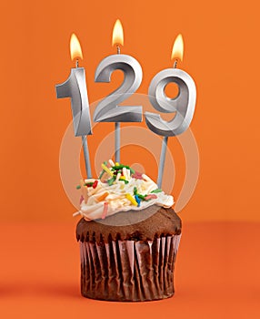 Birthday cupcake with number 129 candle - Orange color background
