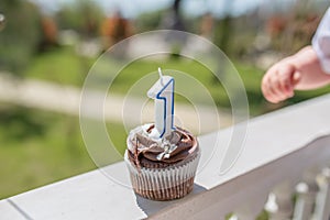 Birthday cupcake with number one candle with little child`s hand on grass background