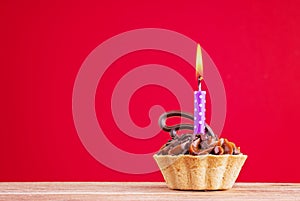 Birthday cupcake on red background with copy space. Caramel cupcake with one purple candle