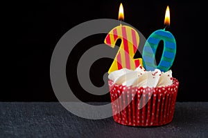 Birthday cupcake with red case and number candles showing 20 on grey slate set against black background.