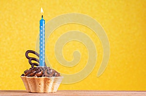 Birthday cupcake on yellow background with copy space. Caramel cupcake with one blue candle