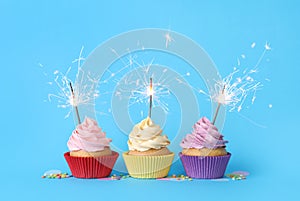 Birthday cupcakes with burning sparklers and sprinkles on light blue background
