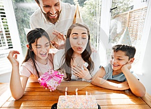 Birthday, family and celebration with a woman blowing the candles on her cake. Husband and kids spoiling mom and making