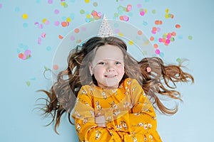 Birthday girl lies on a floor arms-crossed with confetti pieces over her head