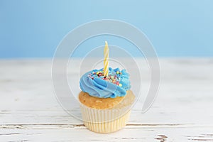 Birthday greeting concept. Yellow candle on muffin, cupcake. Blue background