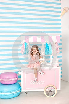 Birthday and happiness concept - happy little girl sitting on a trolley with ice cream and sweets against the background of a cand