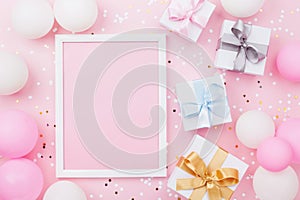 Birthday or holiday mockup with frame, gift box, pastel balloons and confetti on pink table top view. Flat lay composition.