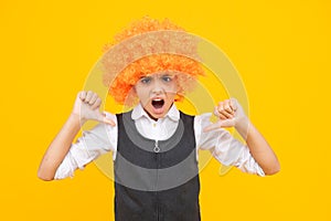 Birthday kids party. Funny kid in curly clown wig  on yellow background. Angry teenager girl, upset and unhappy