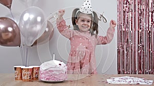 Birthday of a little girl. Child dances for joy. Beautifully decorated room, a cake, a shower of glittery confetti.