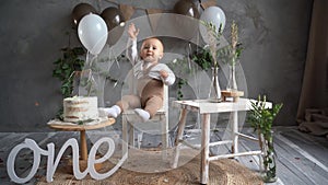 birthday one year old kid, toodler sitting on a chair near cake balloons, confetti pours on the boy child laughing