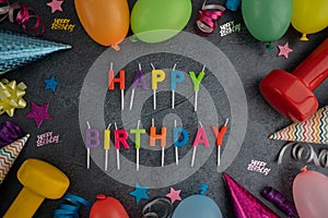 Birthday party composition. Gym dumbbells, colorful balloons, decorations and cake candles.