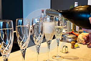 Birthday party, pouring of brut champagne bubbles cava or prosecco wine in tulip glasses with kitchen on background