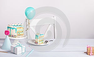 Birthday party setting with slice of cake and decorations on a light grey white background