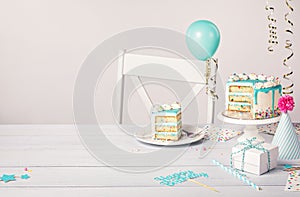 Birthday party table setting with slice of vanilla confetti cake and decorations on a light grey white background