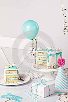 Birthday party table setting with slice of vanilla confetti cake and decorations on a light grey white background