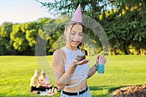 Birthday, teenage girl in festiv hat with cake and candle at outdoor party